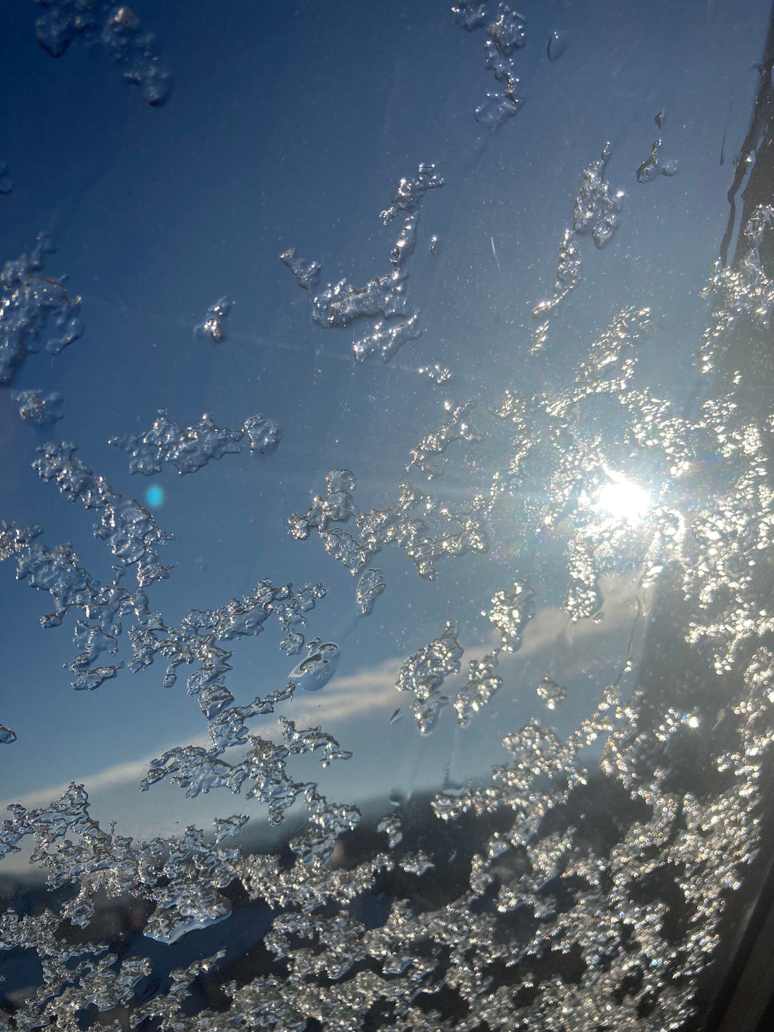 Glitzernde Eiskristalle auf einer Fensterscheibe, im Hintergrund scheint die Sonne hindurch