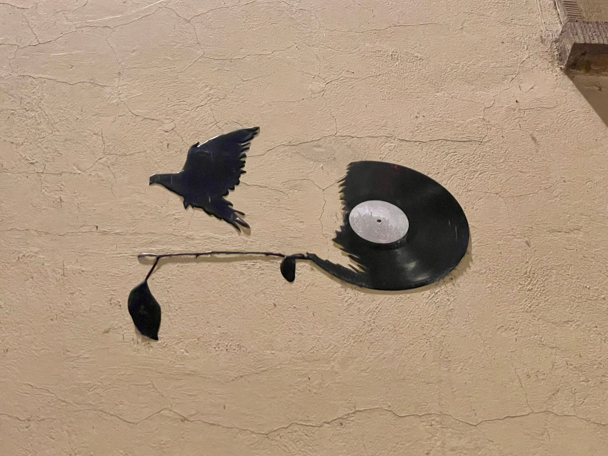 Eine Schallplatte hängt an einer Hauswand in Strasbourg, jedoch ist der linke Teil der Platte abgetrennt, aus den Versatzstücken entschwingt sich ein Vogel, er fliegt davon. (C) Herr Montag.