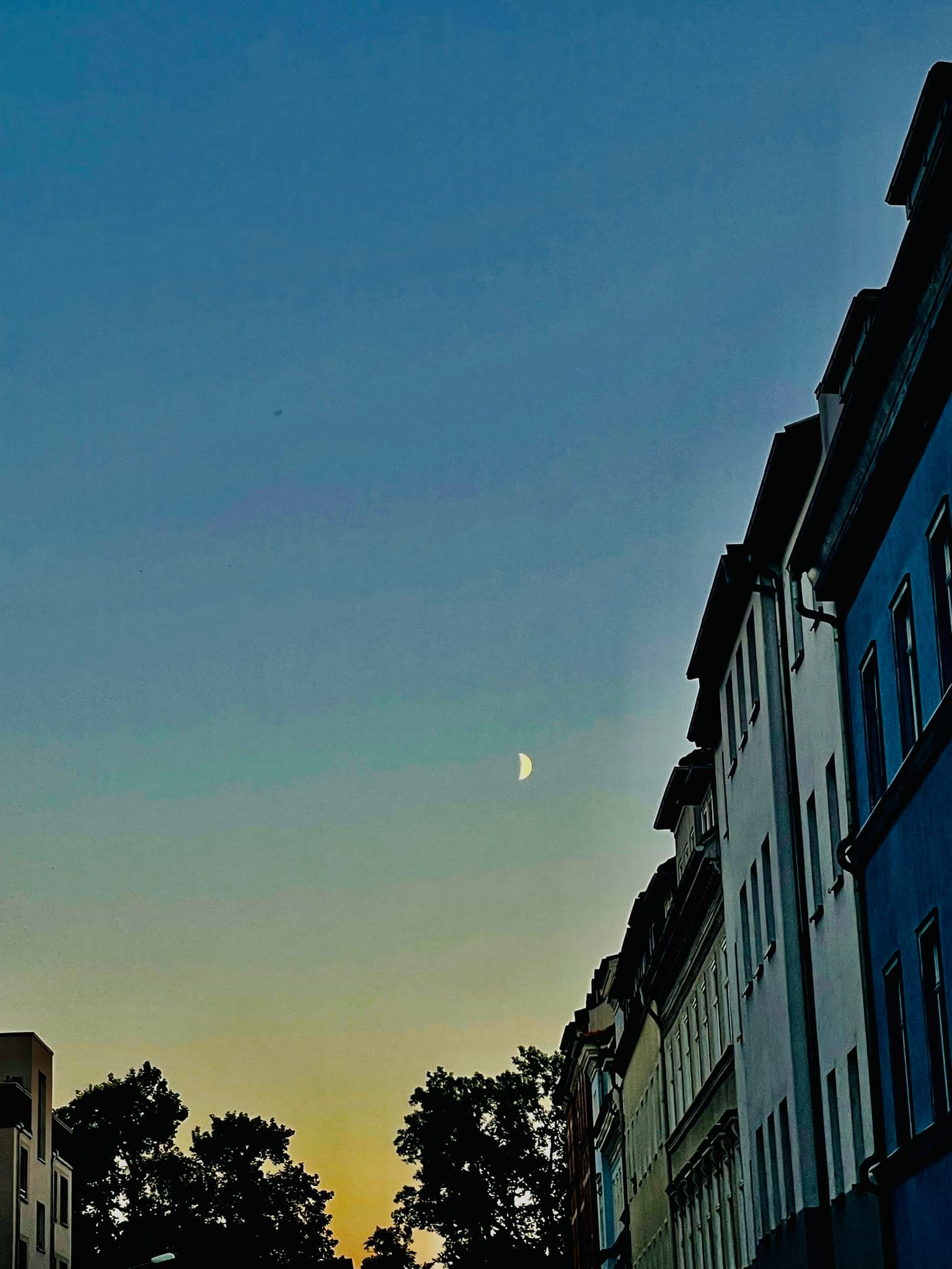 Der Mond als Sichel über der Stadt, rechts sieht man Hausfassaden aus der Gründerzeit. (C) Herr Montag.