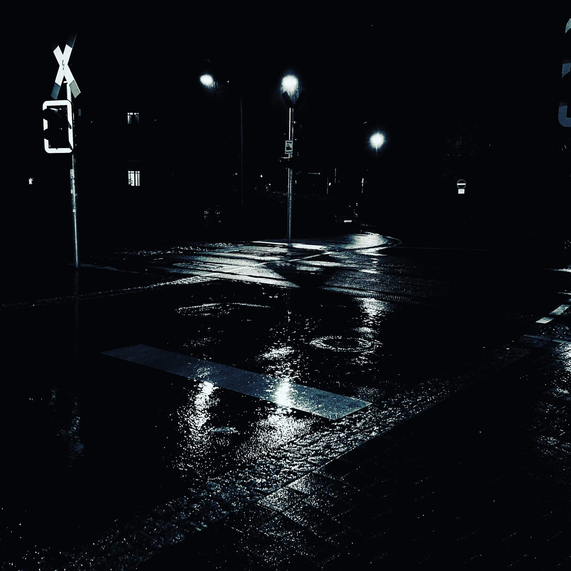Eine Straße im Regen, drei Laternen leuchten, es ist sehr düster