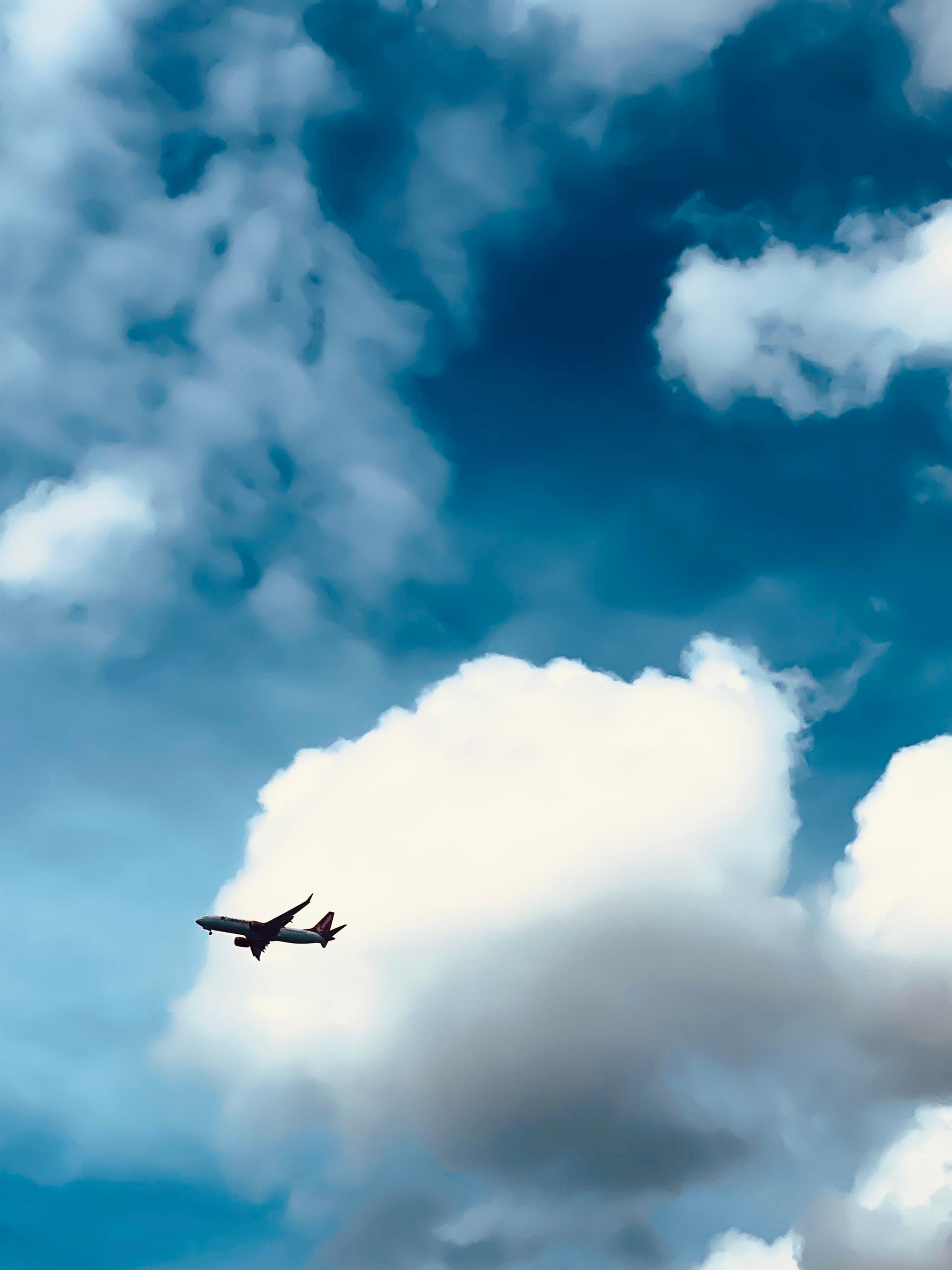 Ein Flugzeug fliegt am Himmel, im Hintergrund sind große, weiße Wolken, dazwischen ist es blau