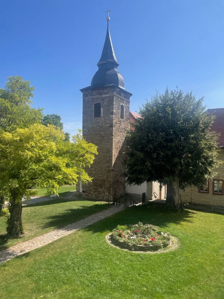 Grüner Rasen, wunderschönes Spätsommer-Licht, alte Burg Mauern – es ist ein Kloster. Im Hintergrund sieht man eine Kirchturmspitze