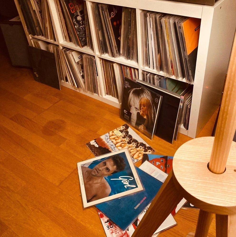 Ein Schallplattenregal und diverse Schallplatten, sie liegen auf einem Laminatboden. Sie liegen etwas übereinander, aber man kann erkennen um welche Bands es sich handelt. Ganz oben Robert Görl mit seinem Solo Debüt. The Cure liegen dort herum genau so wie NICO oder Depeche Mode.